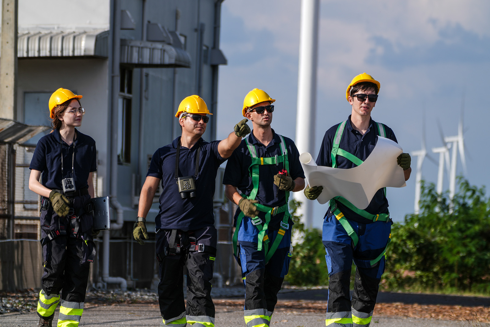 Fire medarbeidere med verneutstyr diskuterer planer under en befaring ved et industrianlegg.