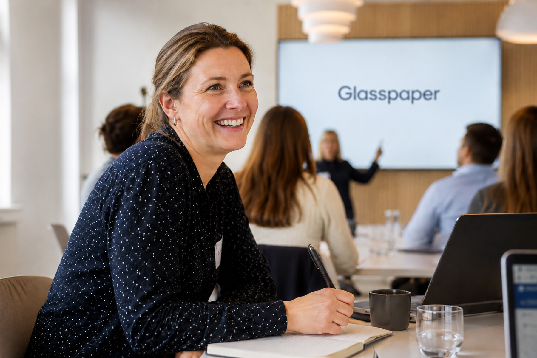 Smilende kursdeltaker på workshop i endringsledelse hos Glasspaper, sittende med notatbok i et moderne kursrom.
