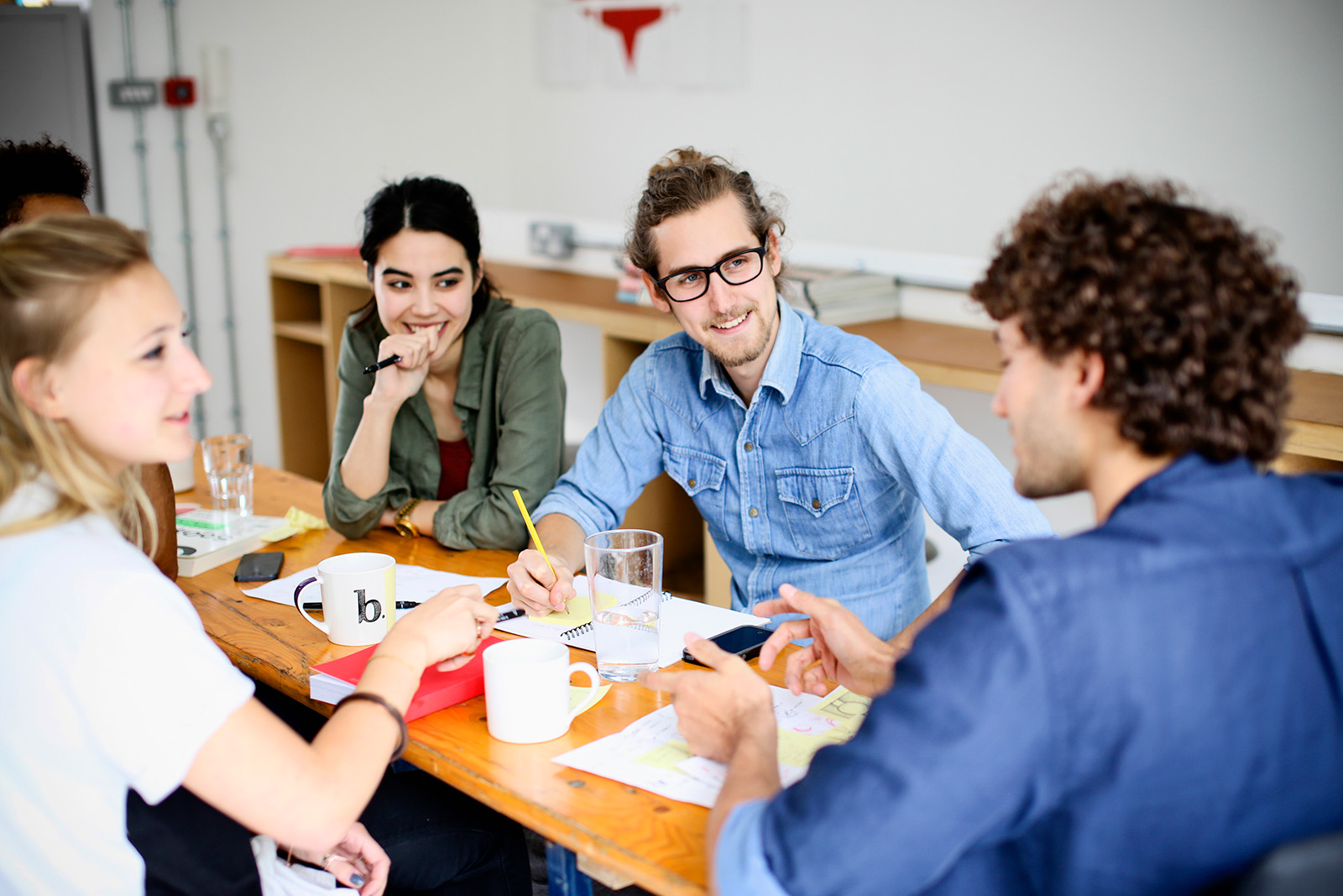 Fire kolleger diskuterer ideer rundt et bord med notater og arbeidsmateriell.